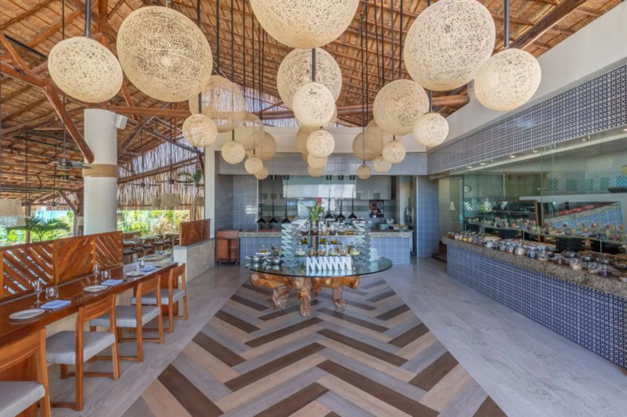 A bright and airy restaurant with a buffet, a thatched roof, and large wicker light fixtures.