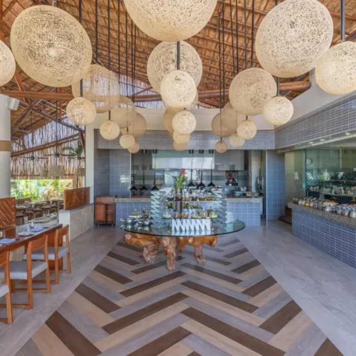 A bright and airy restaurant with a buffet, a thatched roof, and large wicker light fixtures.