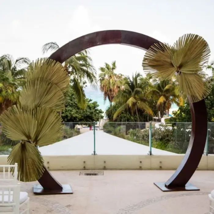 A terrace wedding ceremony venue with an arched floral arrangement and a view of the beach.