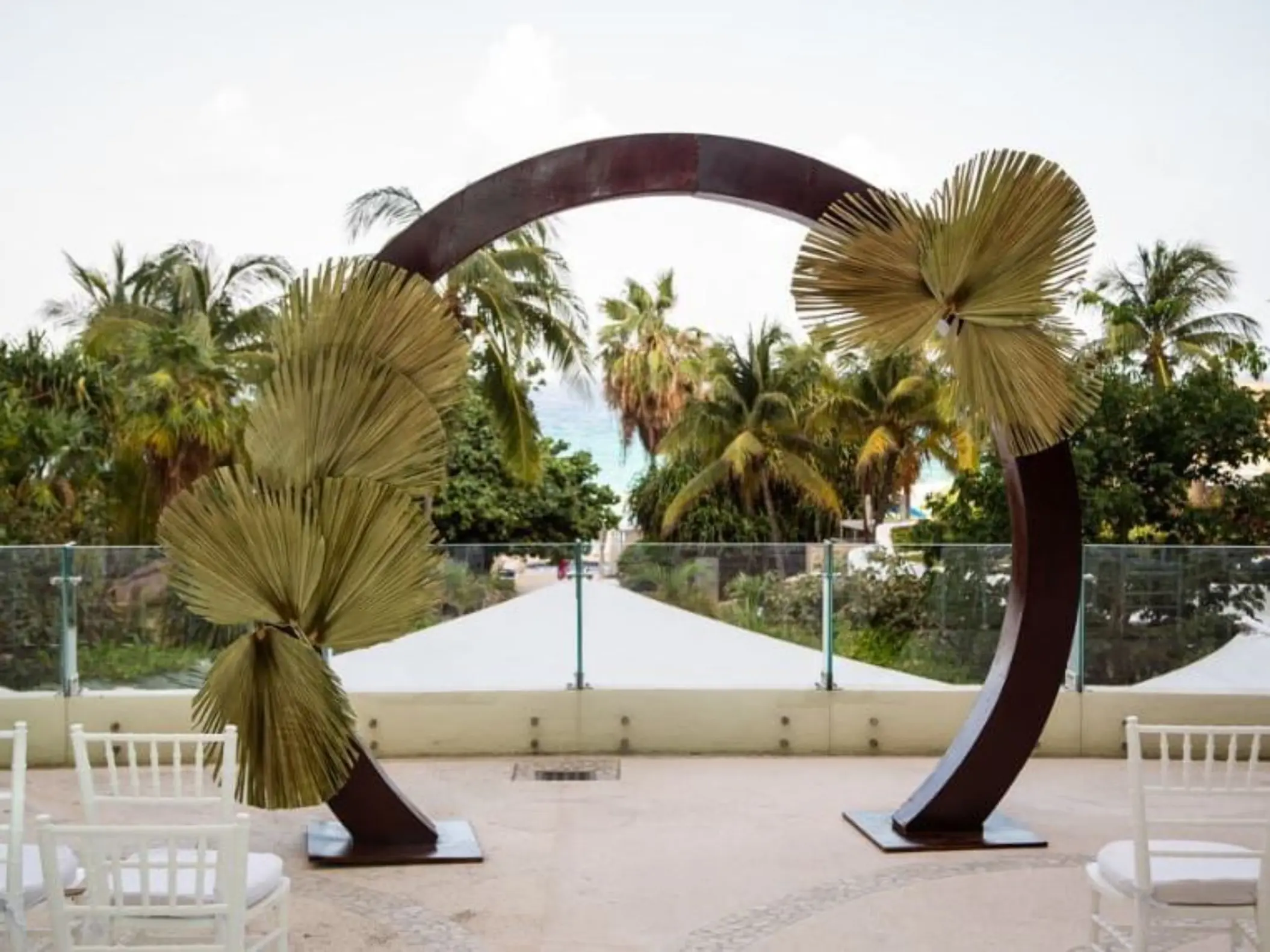 A terrace wedding ceremony venue with an arched floral arrangement and a view of the beach.