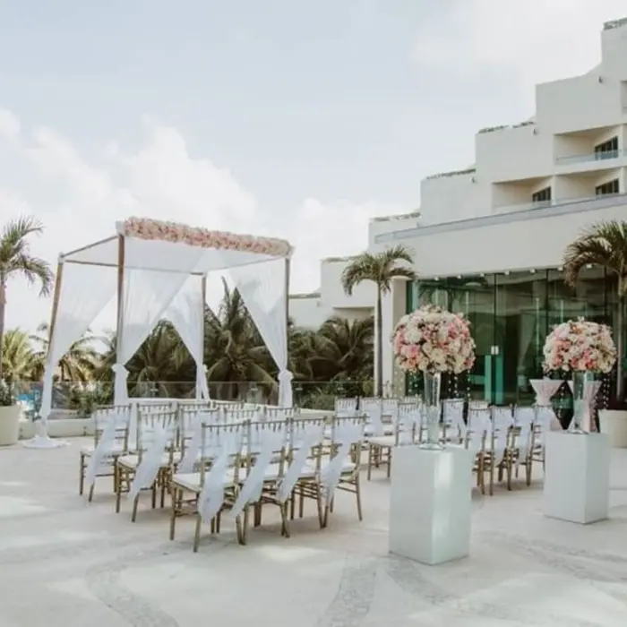 Outdoor wedding venue on a terrace with white chairs, a floral arch, and a view of the resort building.