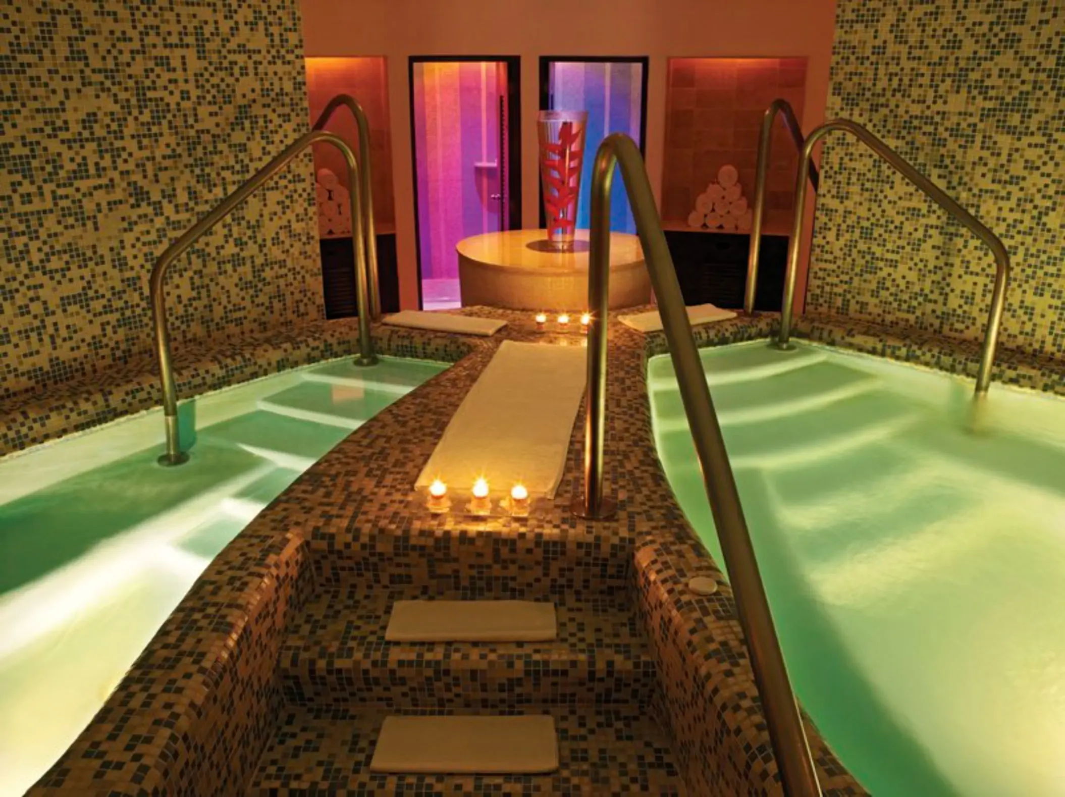 An indoor spa area with tiled pools, lit by warm, inviting lights and candles on the walkway.