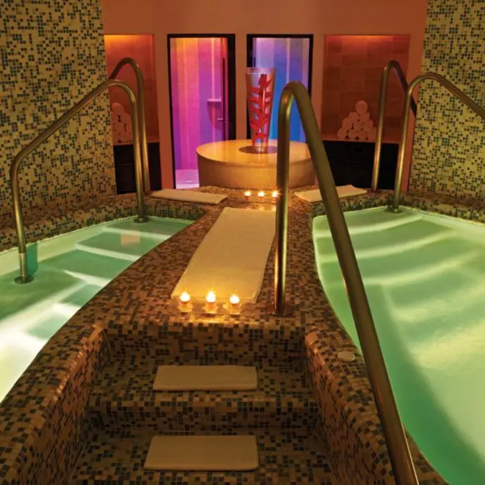 An indoor spa area with tiled pools, lit by warm, inviting lights and candles on the walkway.