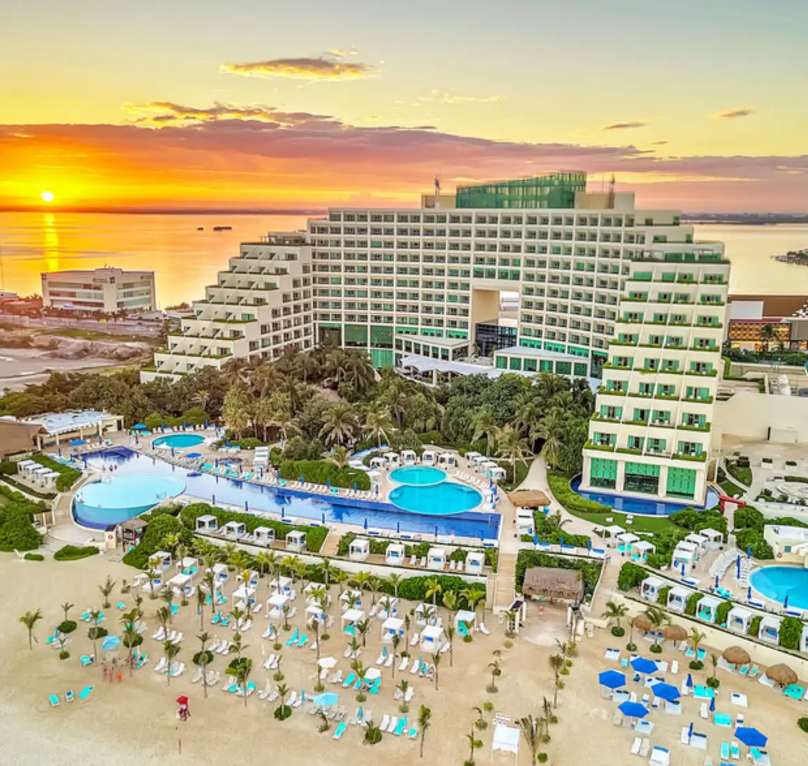 An aerial view of the Live Aqua Cancun resort, showing the building, pools, and beach at sunset.