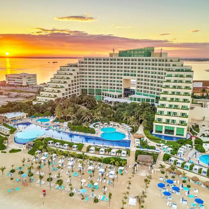 An aerial view of the Live Aqua Cancun resort, showing the building, pools, and beach at sunset.