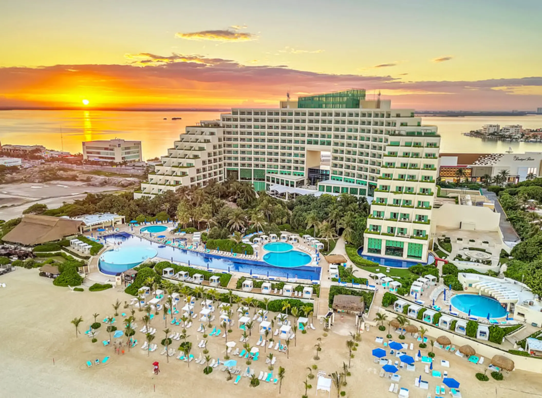 An aerial view of the Live Aqua Cancun resort, showing the building, pools, and beach at sunset.