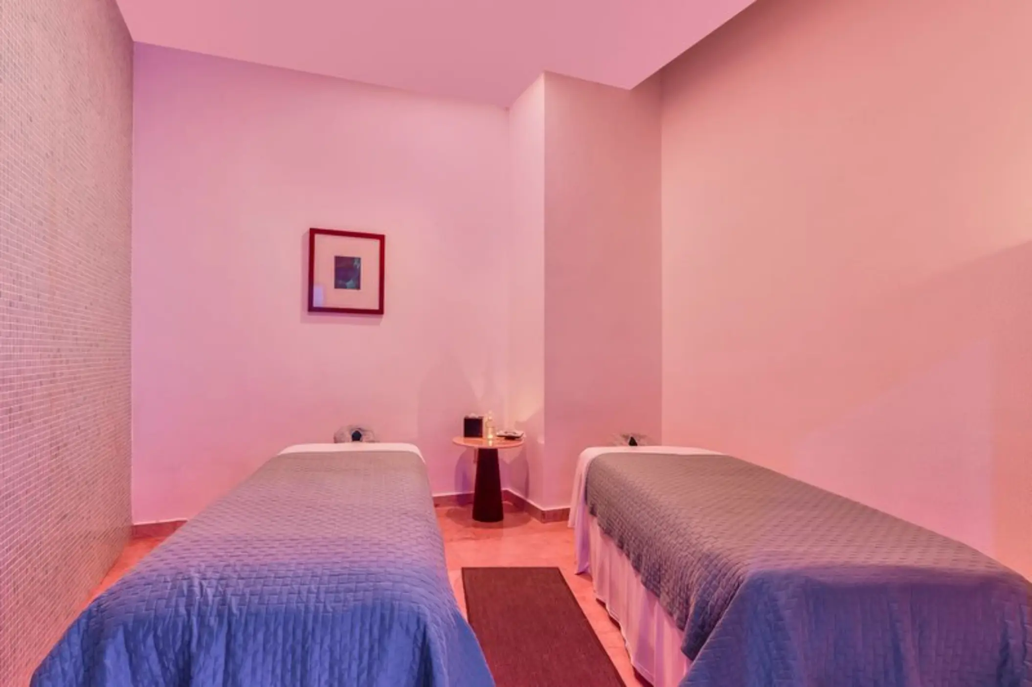 A spa treatment room with two massage tables, soft lighting, and a small side table.