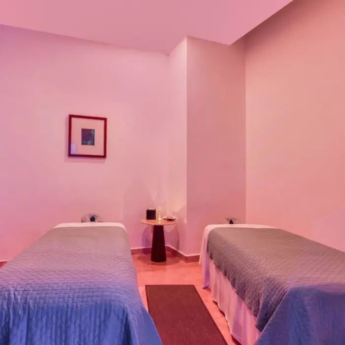 A spa treatment room with two massage tables, soft lighting, and a small side table.