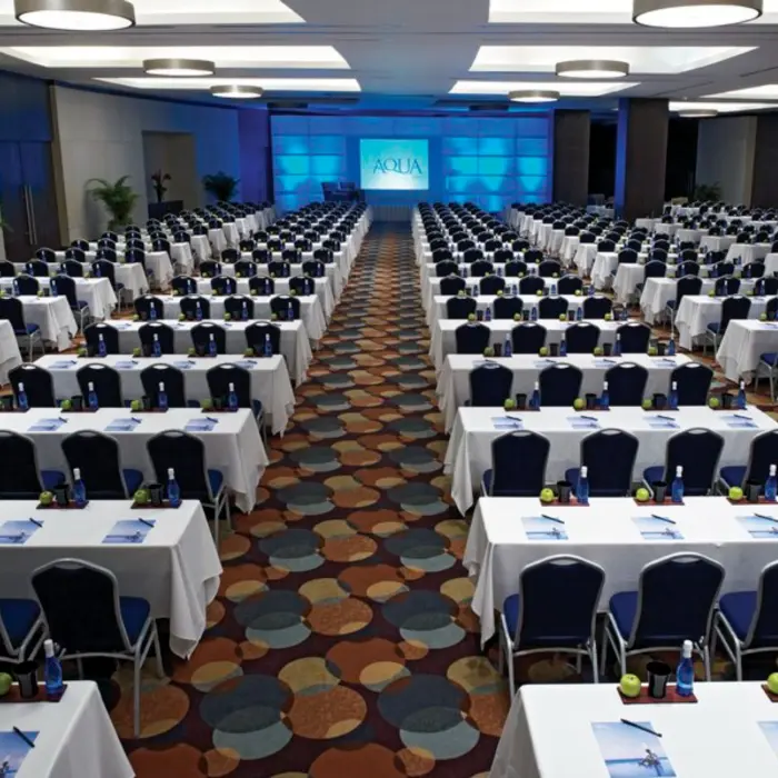A large conference room set up for a meeting with rows of tables, chairs, and a screen.
