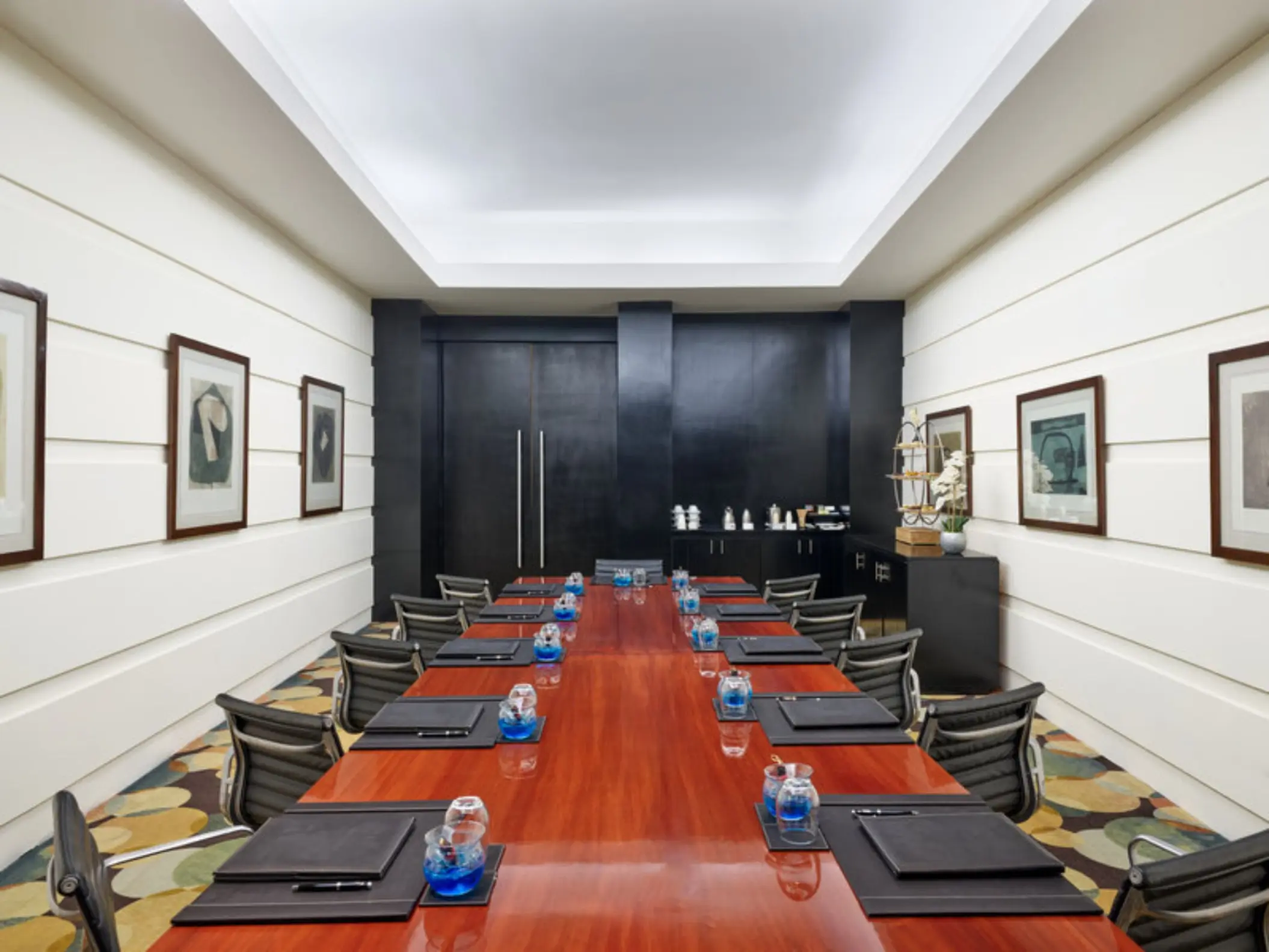 An indoor meeting room with a long wooden table, black leather chairs, and framed artwork on the walls.