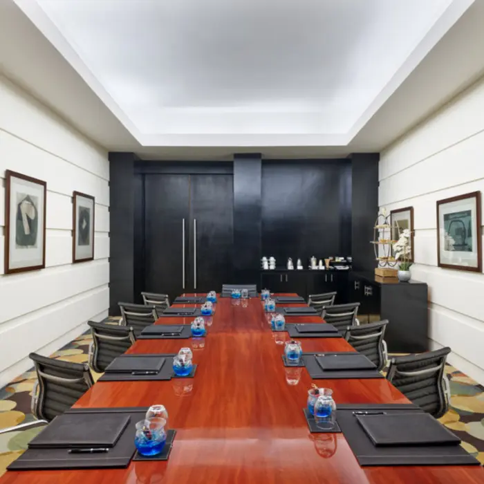 An indoor meeting room with a long wooden table, black leather chairs, and framed artwork on the walls.