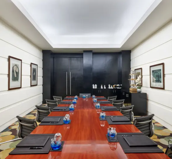 An indoor meeting room with a long wooden table, black leather chairs, and framed artwork on the walls.