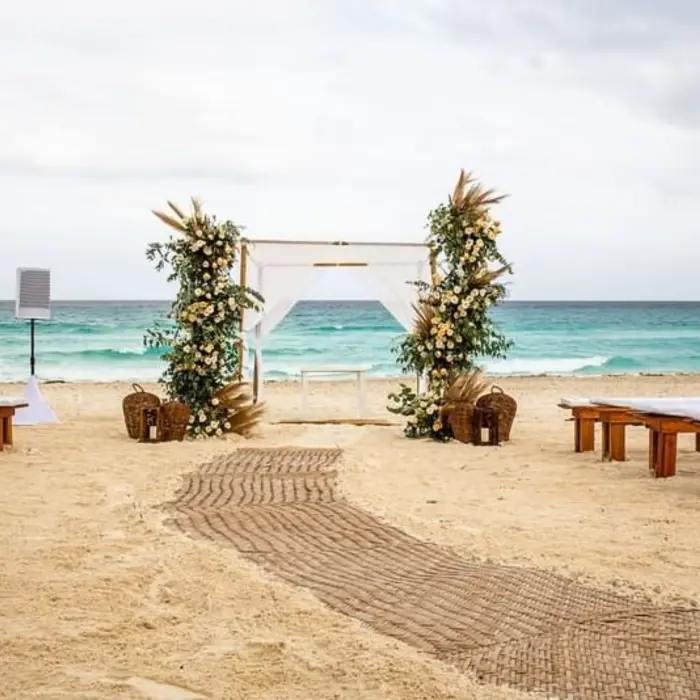 A wedding venue on the beach with a white gazebo, floral arrangements, and benches on the sand.