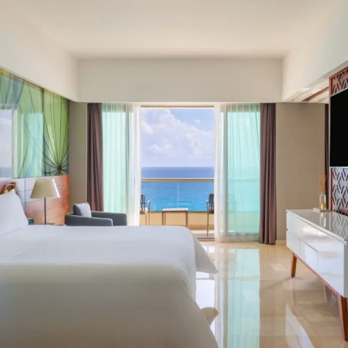 A modern hotel room with a balcony that has a beautiful view of the clear blue ocean.
