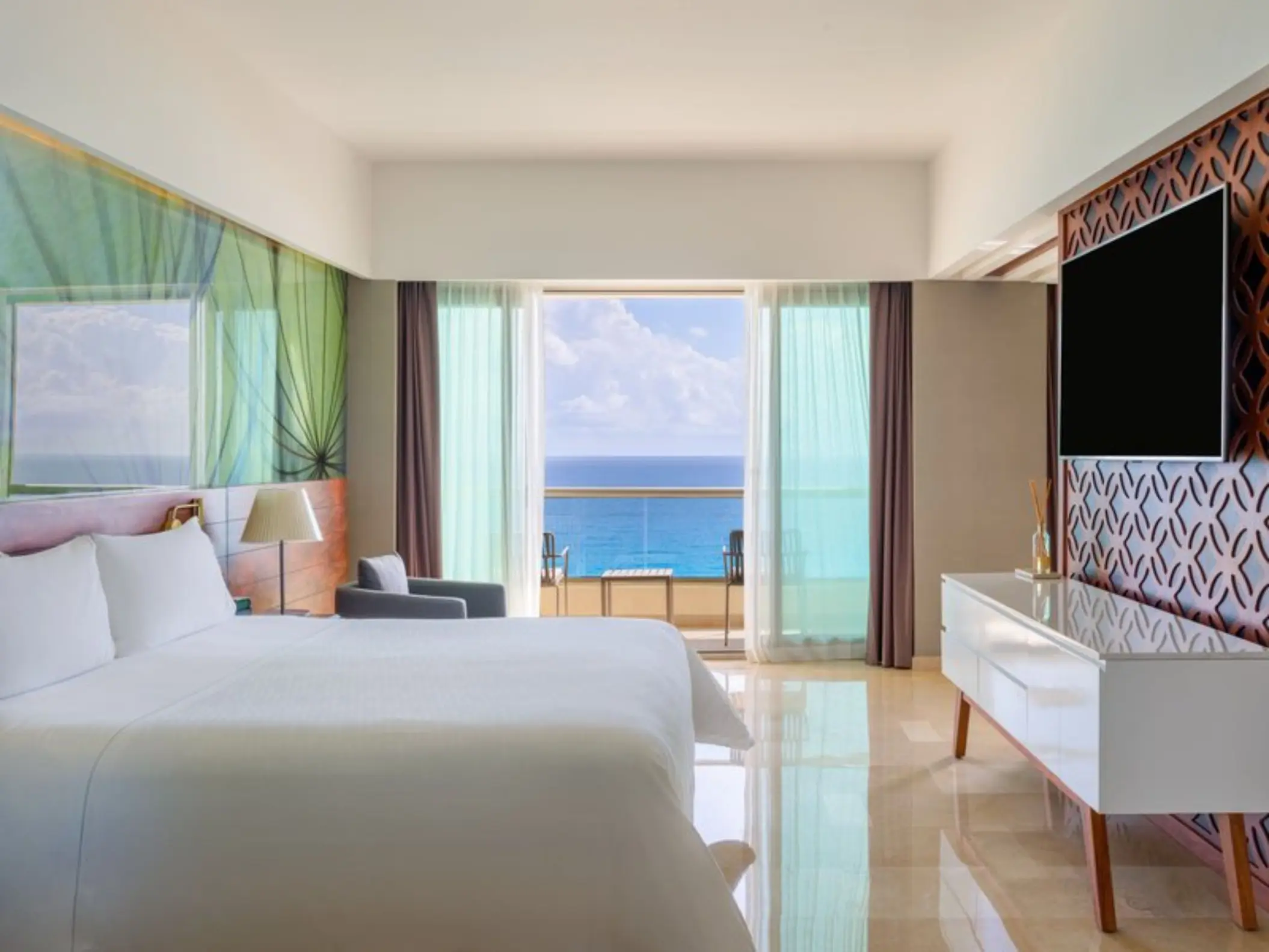 A modern hotel room with a balcony that has a beautiful view of the clear blue ocean.