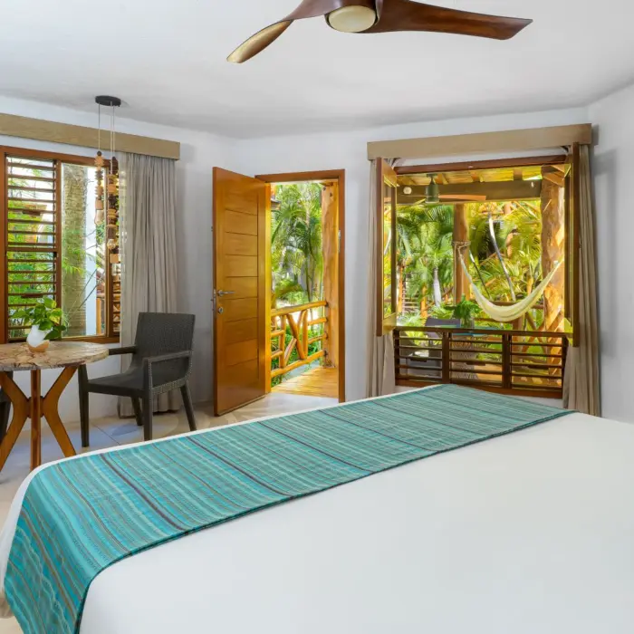 Tropical-inspired guest room with jungle views, rustic furniture, and an open terrace with hammock seating.