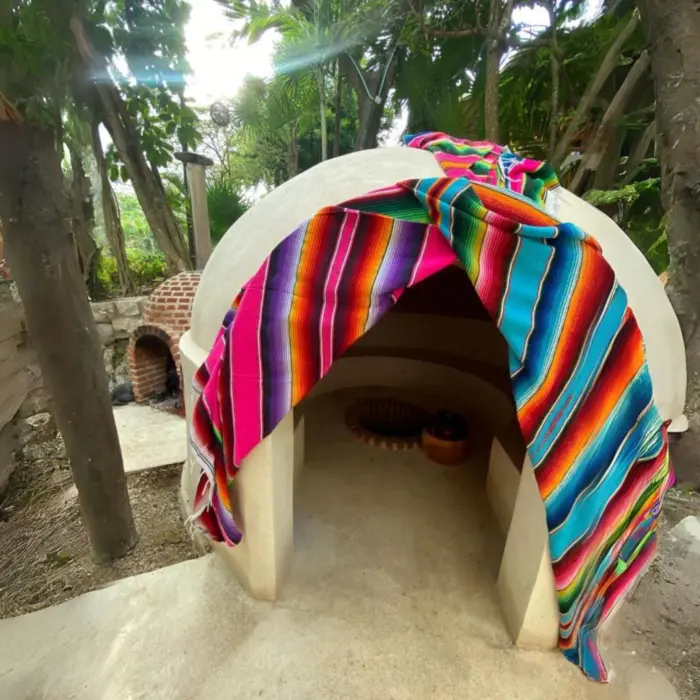 Traditional temazcal dome with vibrant Mexican textile, set in a shaded, leafy outdoor space.