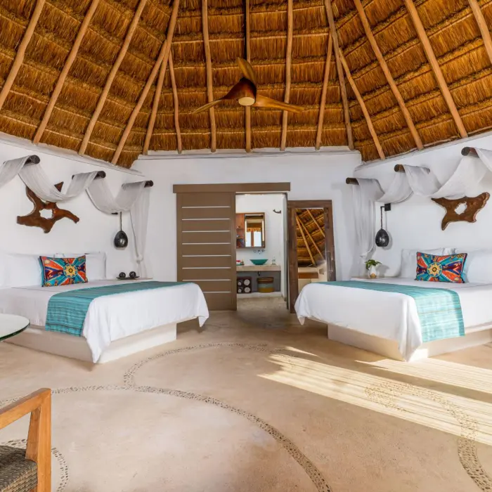 Spacious palapa-style room with two beds, tropical decor, and handcrafted wooden accents at beachfront eco-resort.