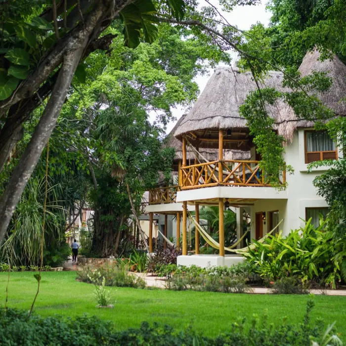 Tropical villa surrounded by lush gardens with private balconies, hammocks, and traditional thatched rooftops.