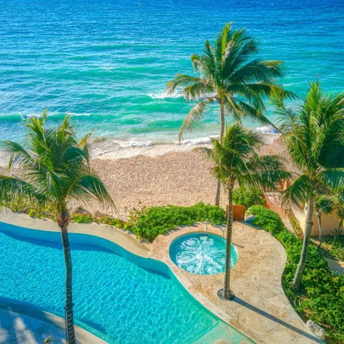 Oceanfront pool with hot tub and swaying palm trees, overlooking a quiet white-sand beach.