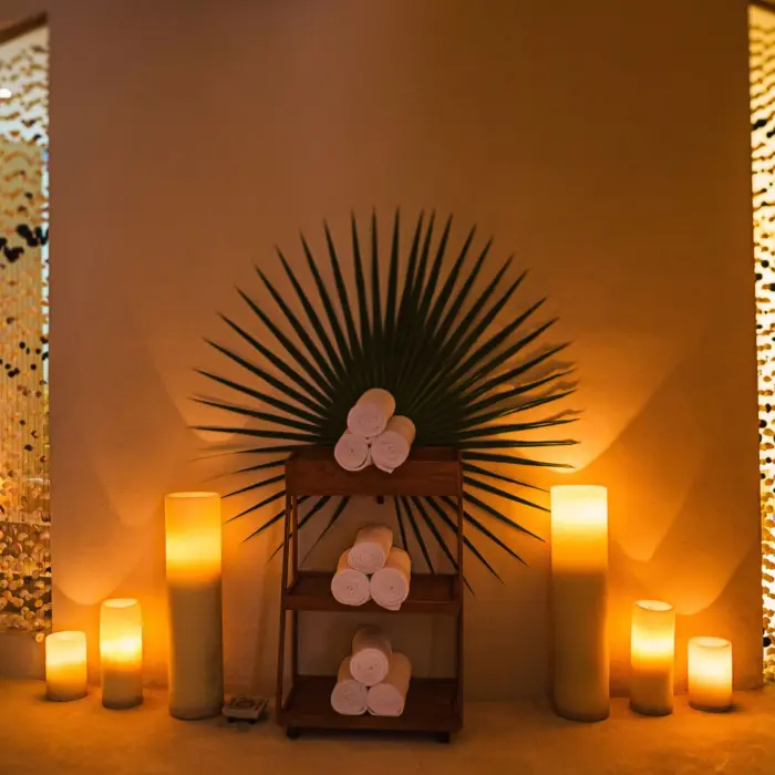 Spa lounge corner with rolled towels, palm leaf decor, and soft candlelight ambiance.
