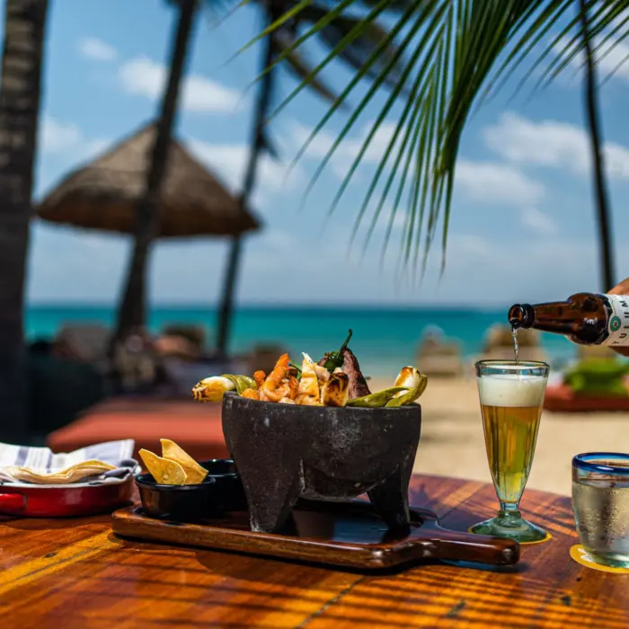 Beachfront lunch with a michelada beer and seafood molcajete under palm trees.