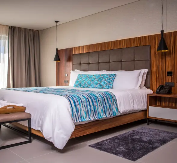 Modern king-size bed with wood paneling, pendant lights, and bright natural light.