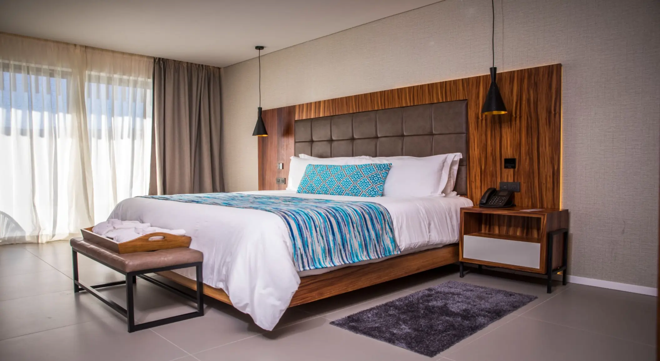 Modern king-size bed with wood paneling, pendant lights, and bright natural light.