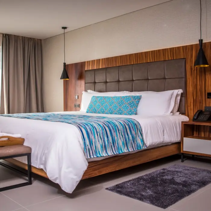 Modern king-size bed with wood paneling, pendant lights, and bright natural light.