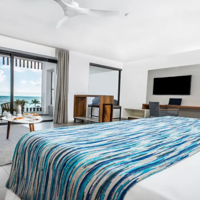 Spacious oceanview room with bed, desk, sofa, and breakfast setup on the balcony.