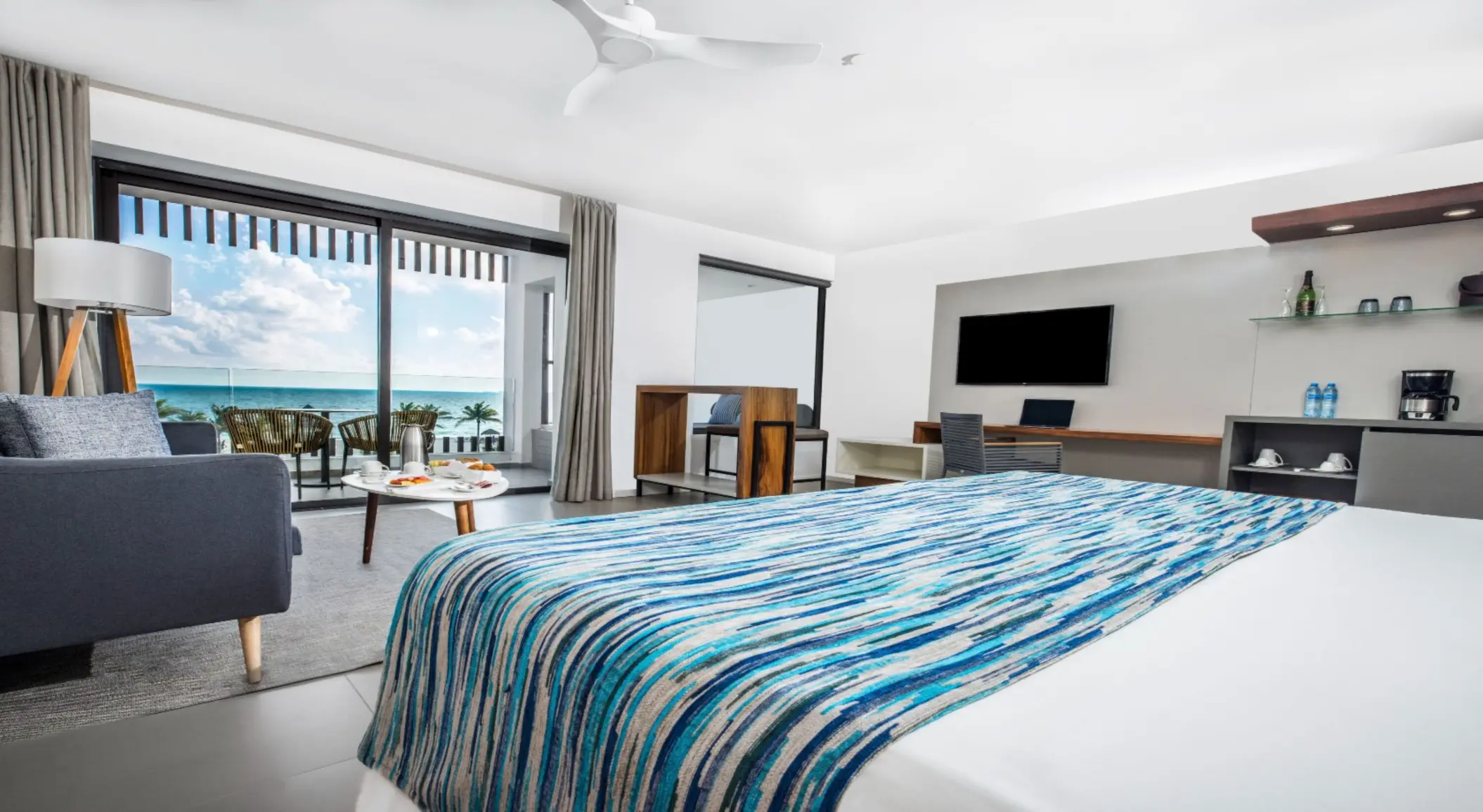 Spacious oceanview room with bed, desk, sofa, and breakfast setup on the balcony.
