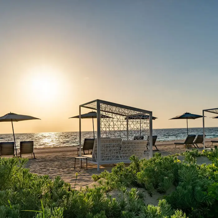 Resort beach with canopy daybeds and umbrellas facing the ocean at sunset.