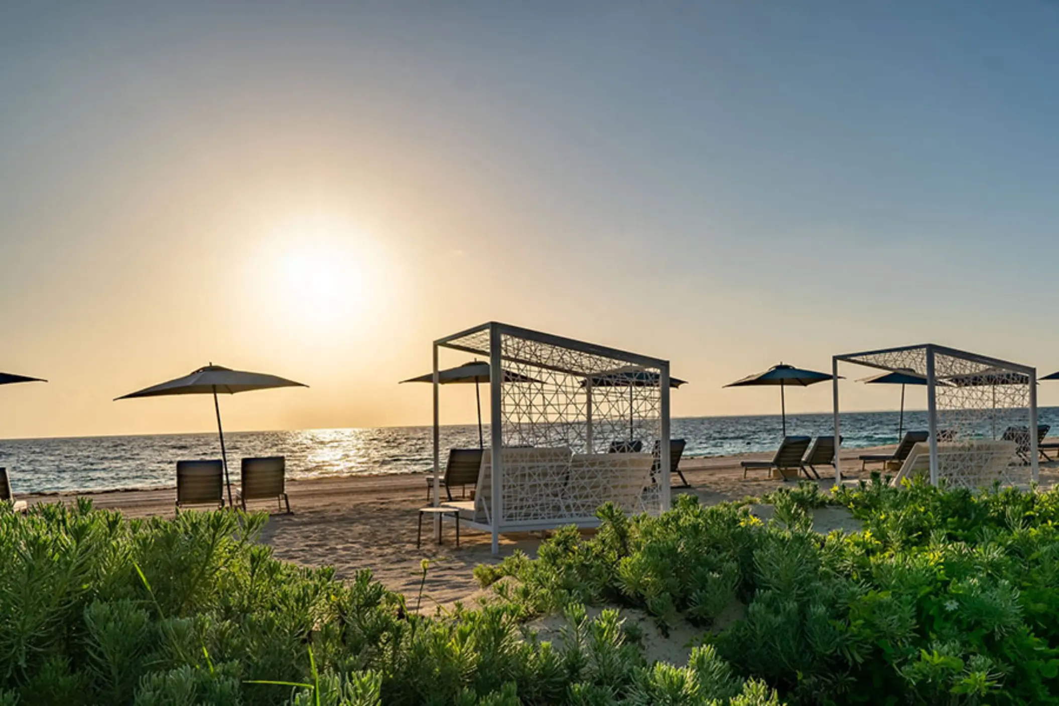 Resort beach with canopy daybeds and umbrellas facing the ocean at sunset.