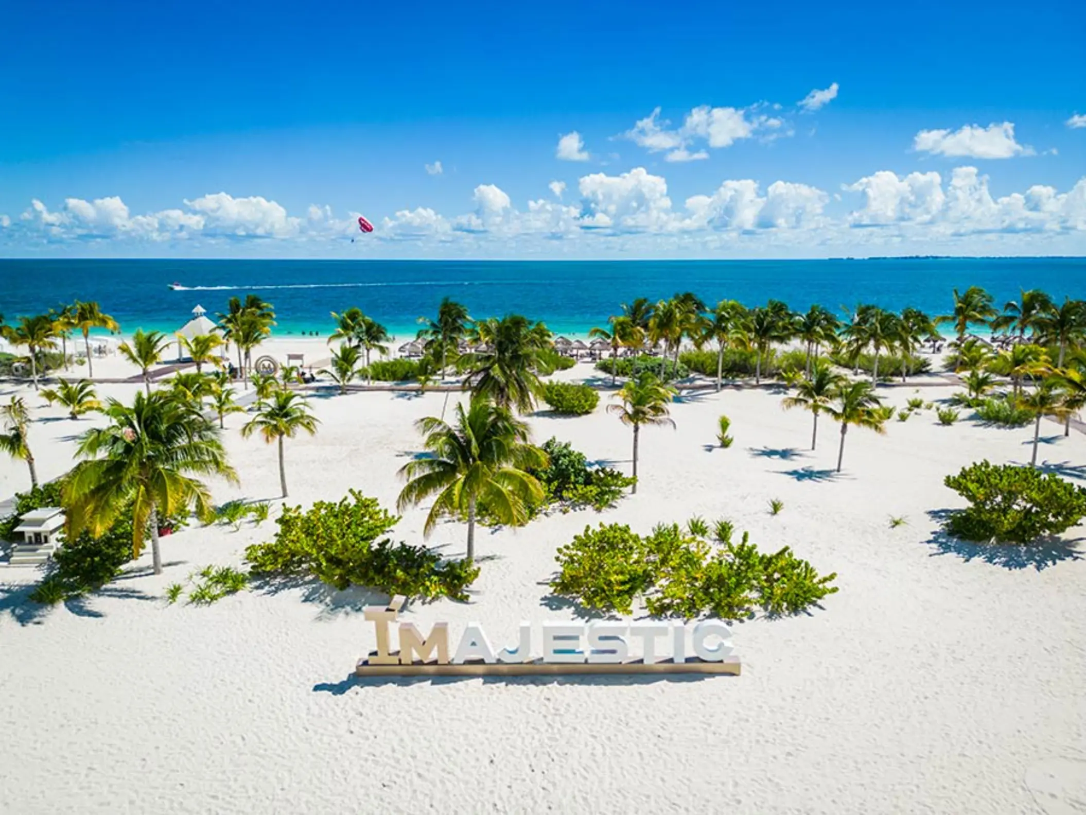 White sand beach with palm trees and large MAJESTIC sign near the shoreline at Costa Mujeres.
