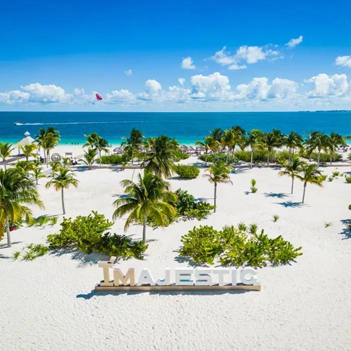 White sand beach with palm trees and large MAJESTIC sign near the shoreline at Costa Mujeres.