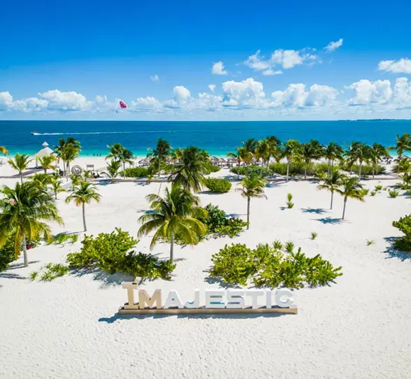 White sand beach with palm trees and large MAJESTIC sign near the shoreline at Costa Mujeres.