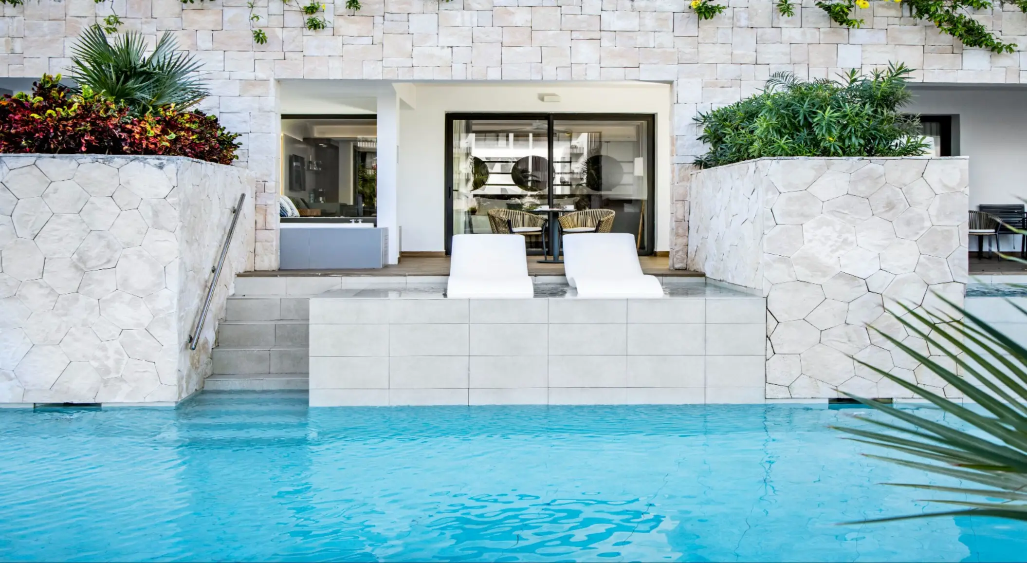 Swim-up suite with poolside loungers and terrace framed by natural stone and tropical plants.