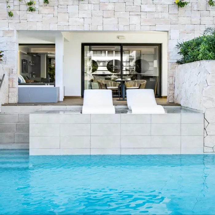 Swim-up suite with poolside loungers and terrace framed by natural stone and tropical plants.
