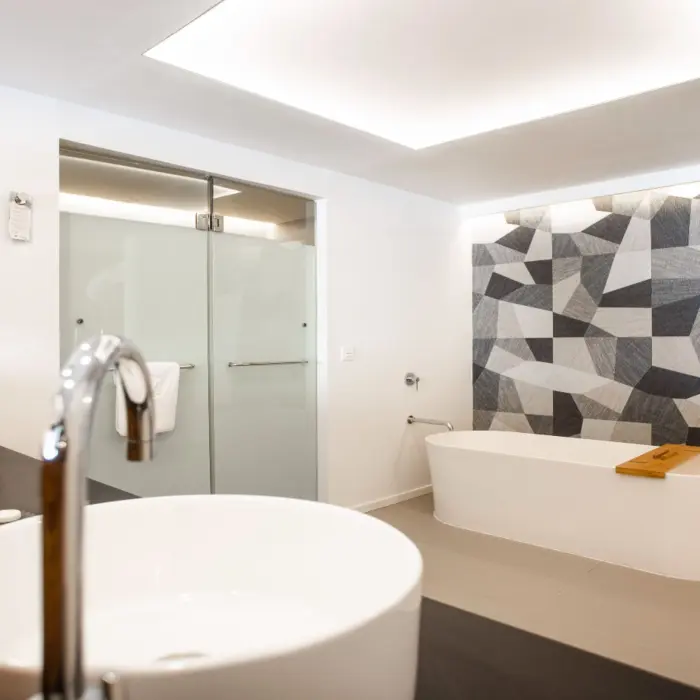 Modern bathroom with twin vessel sinks, geometric wall design, and a standalone soaking tub.