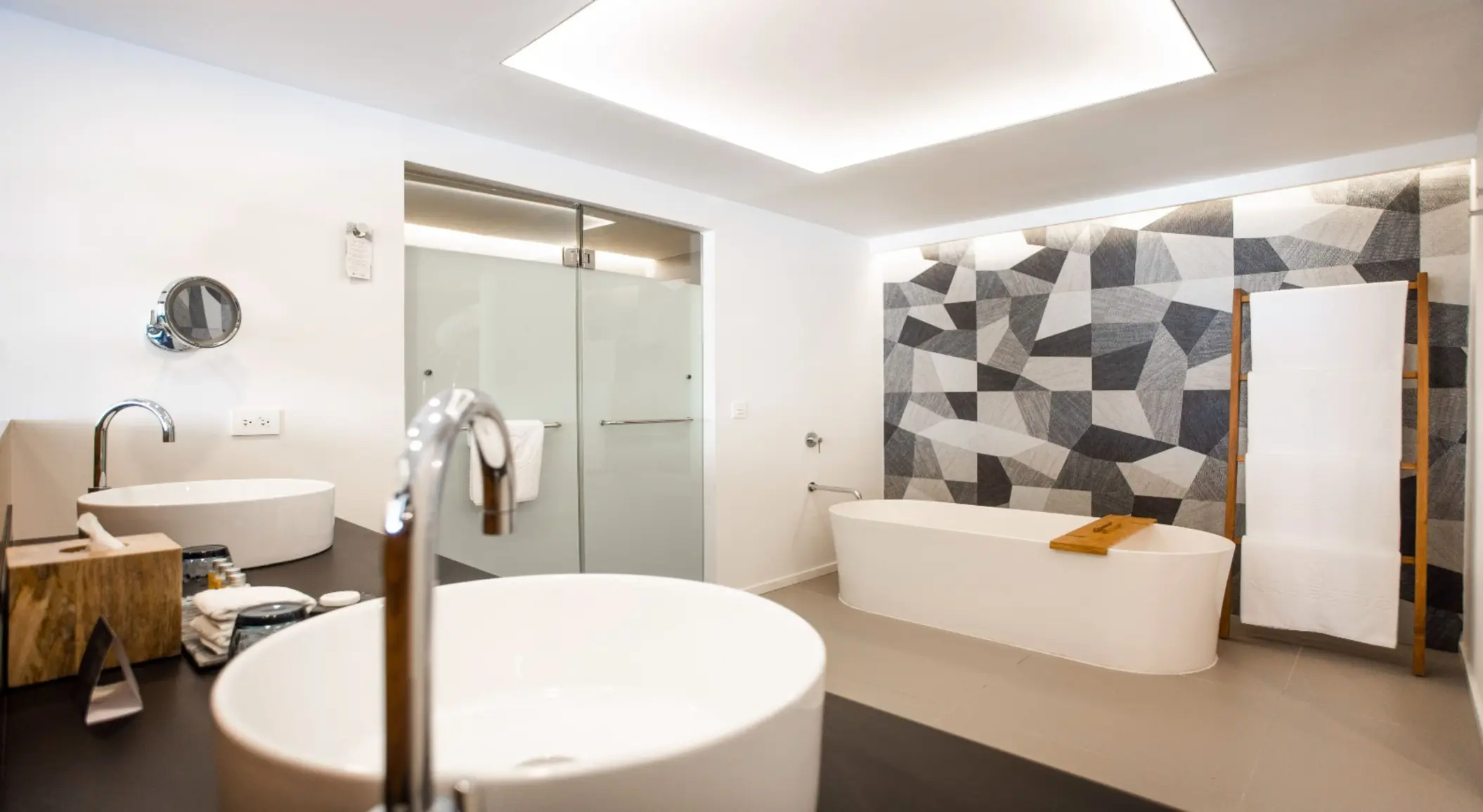 Modern bathroom with twin vessel sinks, geometric wall design, and a standalone soaking tub.