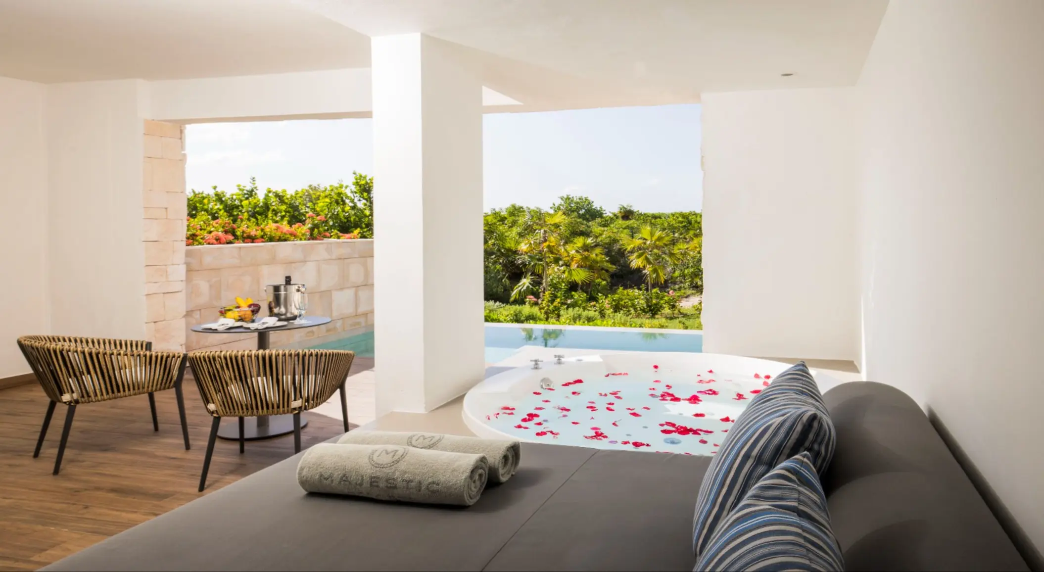 Private terrace with jacuzzi and jungle view, featuring a daybed, chairs, and a breakfast table.