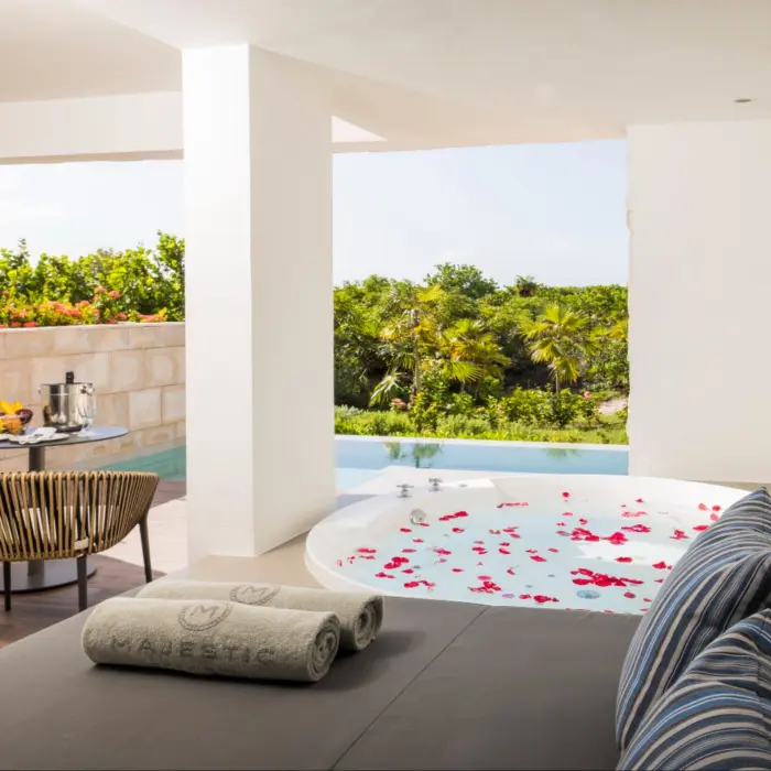 Private terrace with jacuzzi and jungle view, featuring a daybed, chairs, and a breakfast table.