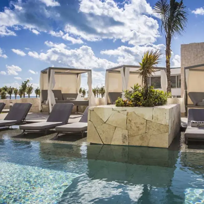 Poolside cabanas and loungers with canopy curtains at Majestic Elegance Costa Mujeres under sunny skies.