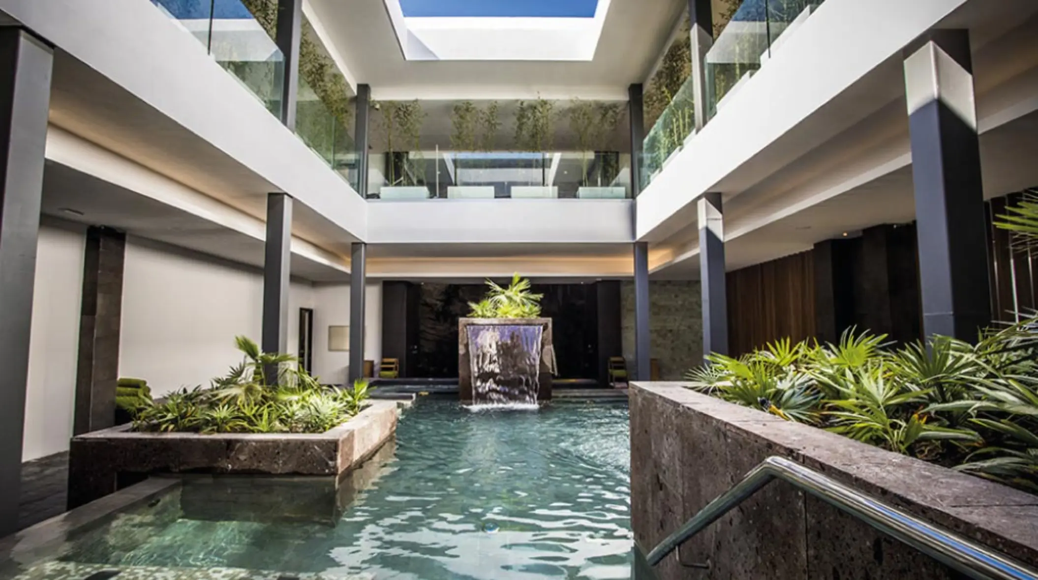 Indoor spa pool with waterfall feature, tropical plants, and natural lighting at Majestic Elegance Costa Mujeres.