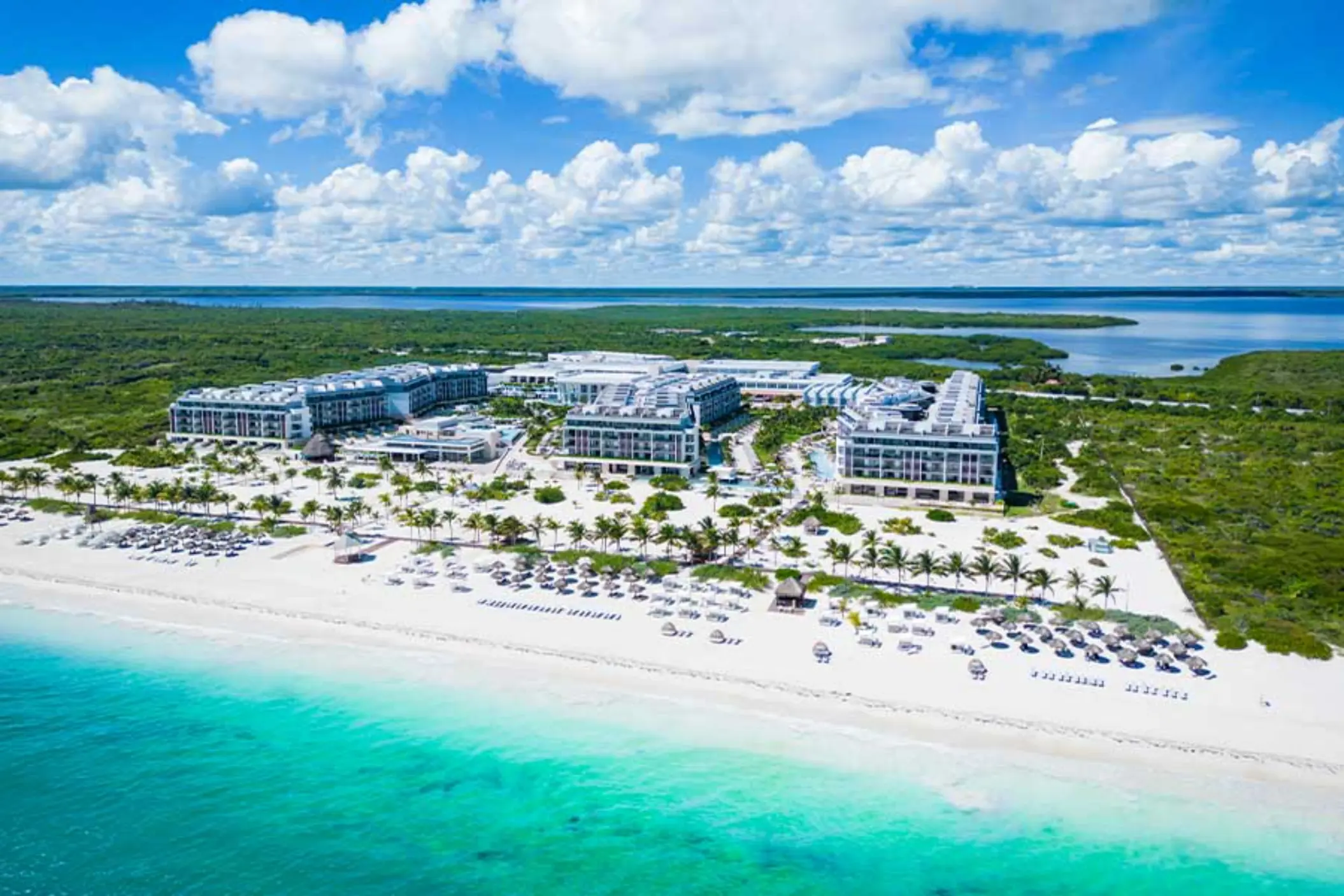 Aerial view of Majestic Elegance Costa Mujeres beachfront resort surrounded by lush greenery and turquoise water.