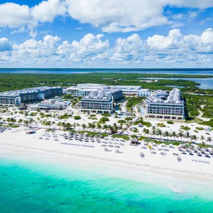 Aerial view of Majestic Elegance Costa Mujeres beachfront resort surrounded by lush greenery and turquoise water.