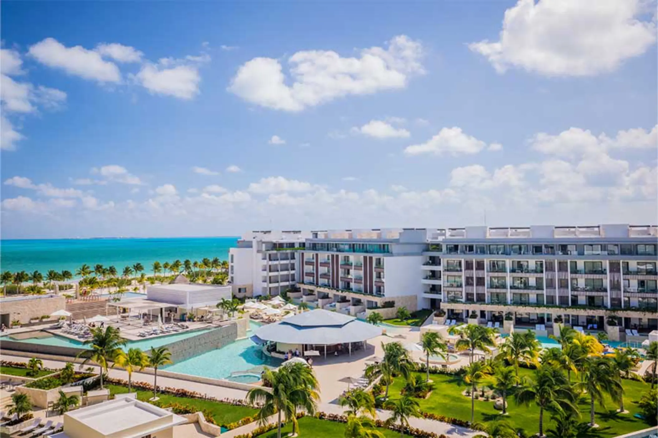 Poolside view of Majestic Elegance Costa Mujeres with ocean backdrop and palm-lined property.