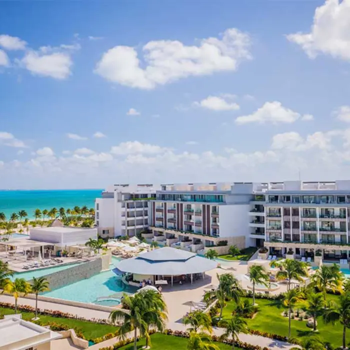 Poolside view of Majestic Elegance Costa Mujeres with ocean backdrop and palm-lined property.