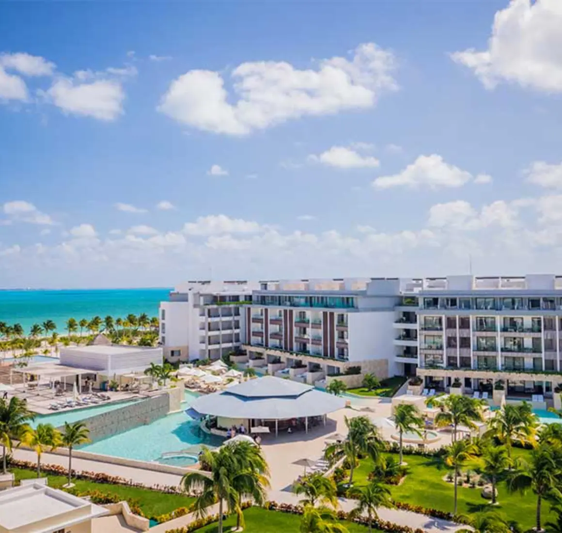 Poolside view of Majestic Elegance Costa Mujeres with ocean backdrop and palm-lined property.