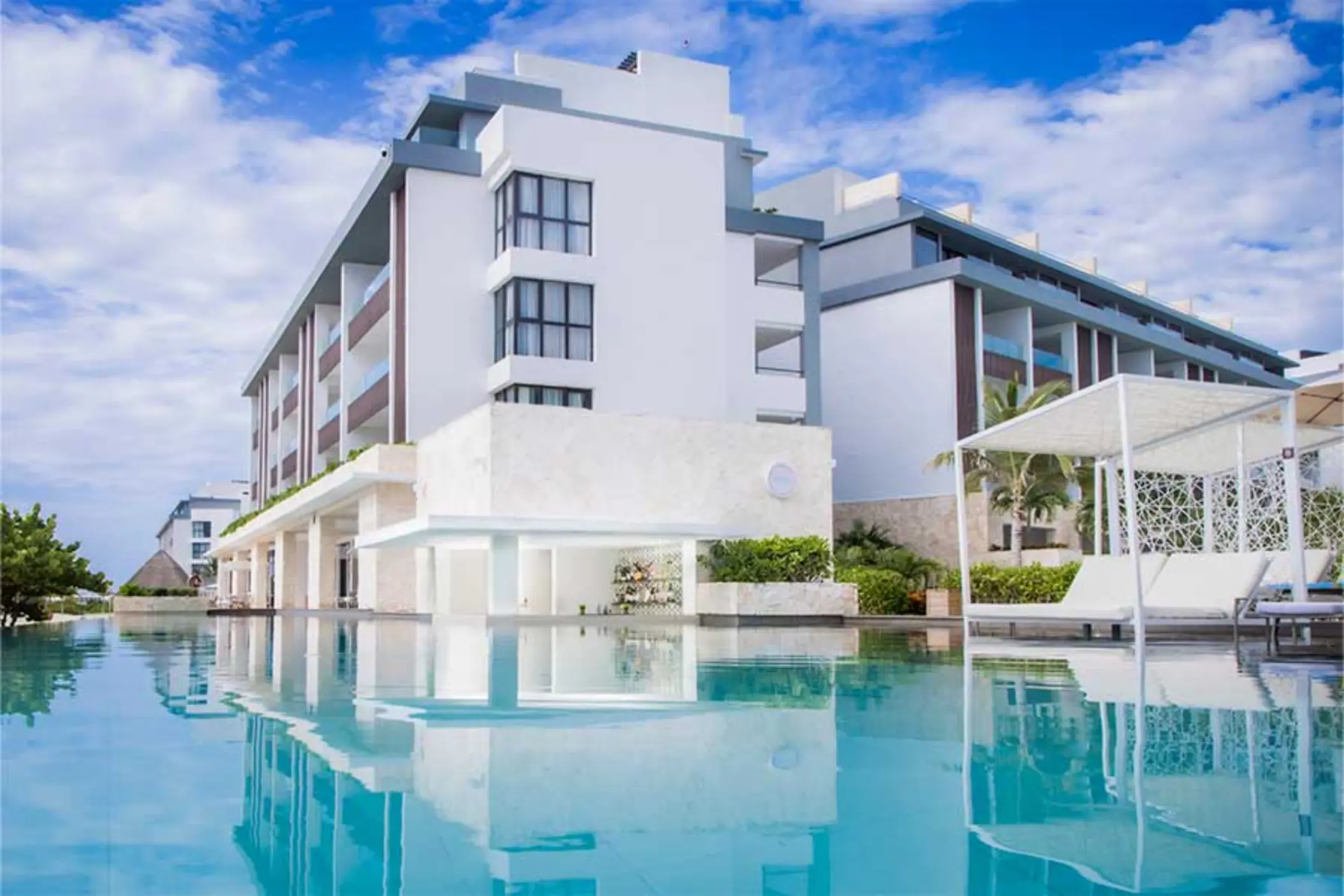 Infinity-edge pool with modern architecture and shaded lounge beds at Majestic Elegance Costa Mujeres.